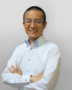 代表者の顔写真(白いシャツで腕を組む笑顔の男性)
